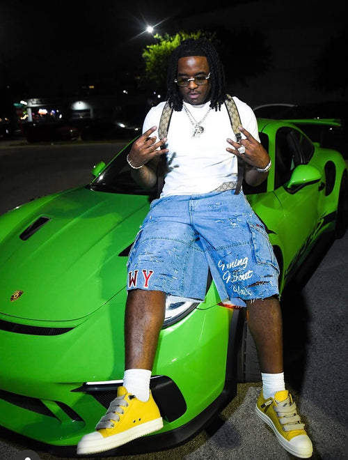 Model wearing WINNINGWITHOUTYOU blue distressed denim shorts in front of green exotic car